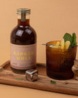 Bottle of 'Ginger Mule' with a cocktail and ginger root on a wooden tray against a beige background
