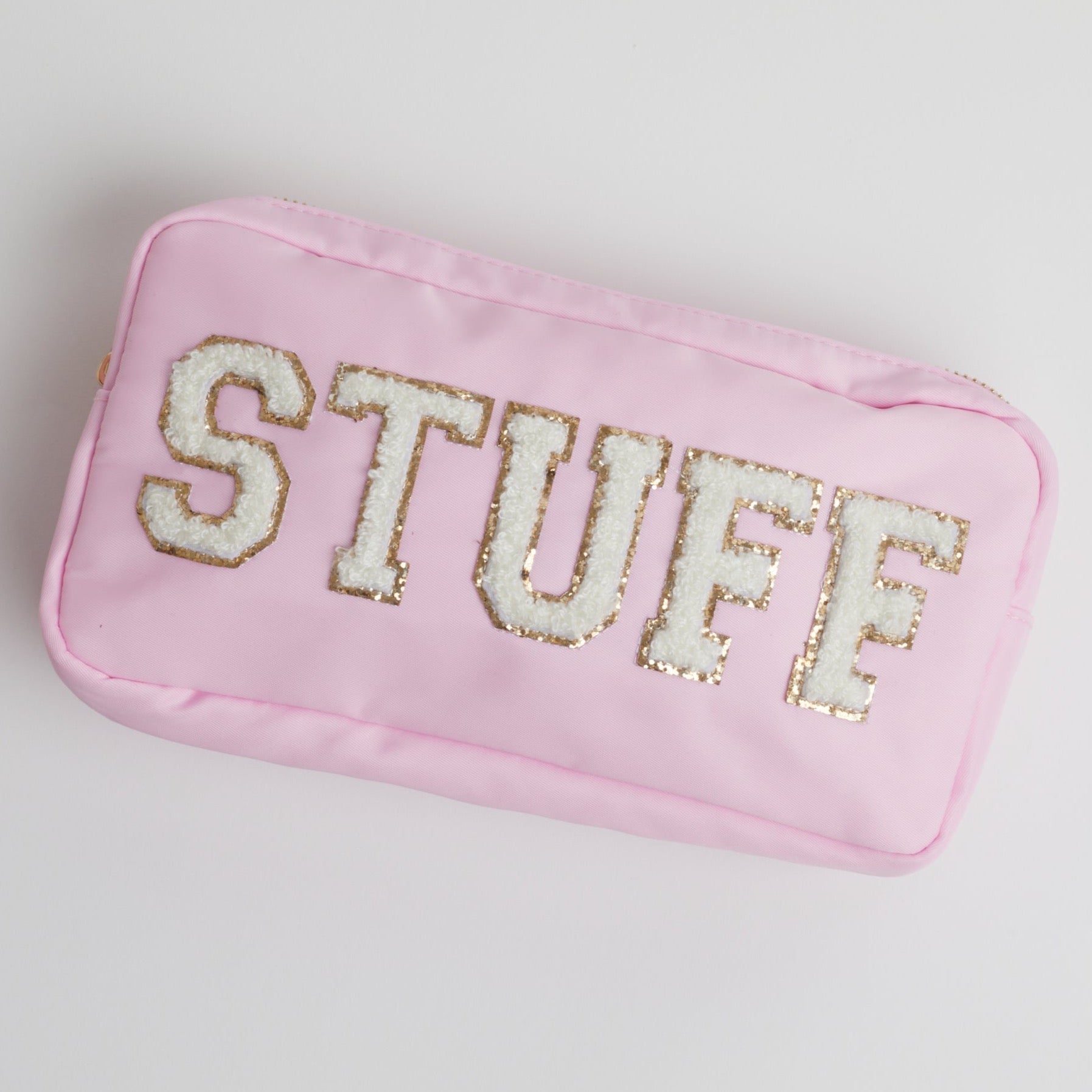 A pink cosmetic bag with white terry cloth letters spelling out "STUFF" on a white background.