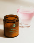 Vice Juice Mini Dew candle in an amber jar with a pink glass in the background.