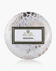 A round decorative box for a Voluspa Mokara coconut wax melt perfume, featuring a white and silver floral lace pattern with a central white label.