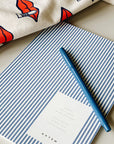 Blue pen on a striped notebook with a partially visible page