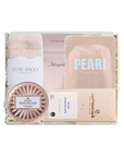 A curated beauty gift set in a white box, featuring a pink towel, a sheet mask labeled 'PEARL BRIGHTING', a rose gold sparkling rose scrub, a chocolate bar, and a moisturizer from the brand moenstruck.