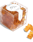 The image shows a package of gummy candies by Sugarfina. The packaging design has a label in the center with the text "Mr." written in a gray, cursive font. Above the text, there's a small, simple bow-tie graphic. Surrounding the label, the gummies are visible through the clear packaging. The gummies are amber-colored and shaped like bears. There are three bears outside of the box pictured to the right of the box.