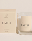 pale beige candle packaging by HAVYN that says FAITH SANTAL COCONUT PETAL next to clear glass candle on the right