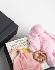 Baby gift set with pink plush toy, book, and hat in a box on a white background