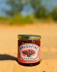 Jar of Bushfire Farms Original Pepper Jelly on a dirt surface with blurred greenery in the background