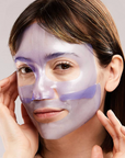 Woman applying a purple facial mask on a plain background