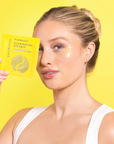 Woman with eye gels under eyes holding a package against a yellow background