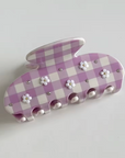 Purple and white checkered hair clip with floral decorations on a light gray background