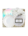 A white eye makeup gift set in a square box with shredded paper filler, featuring a white scalloped eyeshadow sponge, a white fabric scrunchie, a round white doily-style compact with a Nora.