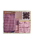 A boxed beauty gift set on a white background, containing a pink and purple houndstooth scarf, a bottle of Kitsch hair perfume, a pink box with a gold logo, a tray of dark brown chocolate-covered candies, and a pink patterned packet labeled 'SWEATER WEATHER'.