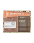 A boxed fragrance gift set from esw beauty, featuring a scented soap candle in a brown plaid tin labeled 'Pumpkin Whimsea', a brown paper card reading 'Tea with Tae', and an orange tube labeled 'esw beauty'. The set is presented in a clear box with shredded paper filler on a white background.