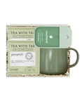 An olive green ceramic mug with a matching green lid sits in a white gift box with shredded paper, next to a printed tea sachet labeled 'TEA WITH TAIWAN' and a green card reading 'touchland'.