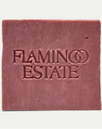 A square bar of dusty rose soap with the brand name 'FLAMINGO ESTATE' embossed on the front, set against a clean off-white background.