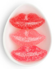 Three sugar-coated lip-shaped gummy candies stacked vertically in a white oval dish on a white background.
