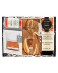 A curated whiskey gift set in a black tray filled with white paper shred, featuring a bottle of Jack Rudy Cocktail Co. Bourbon Cocktail Crèche, a Ritual 75% Aged Bourbon Barrel Aged whiskey bottle, a clear glass tumbler, and a branded box.