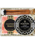A luxury gift set in a white box containing a round tin of Voluspa Crisp Champagne handcrafted cocoa wax, a bar of champagne bears sugarfina soap, and a wooden hair stick with a black and white patterned top.