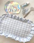 Blue Gingham Ruffle Pouch next to eye masks, face oil, hair clip and tube key.