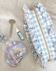 Blue Gingham Ruffle Pouch next to eye masks, face oil, hair clip and tube key.