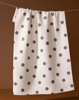 White towel with brown polka dots hanging on a line against a brown background