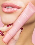 woman wearing light pink lipgloss & holding pink lipgloss tube