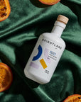 Brightland olive oil bottle on a green fabric background with sliced oranges.
