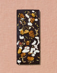 Dark chocolate bar with various toppings on a pink textured background