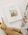 Children's book titled 'Our Little Adventure to the Farmer's Market' with a plush rabbit toy and patterned blanket on a light background.