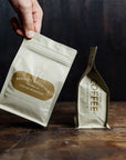 Hand holding a coffee package with 'Bradley Mountain Coffee Roasters' branding on a wooden surface.