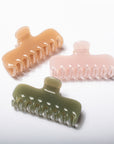Three translucent hair claw clips in peach, pale pink, and sage green, arranged diagonally on a clean white background.