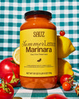 Jar of Sauz Summer Lemon Marinara sauce on a checkered tablecloth with lemons and tomatoes.