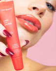 woman wearing cherry red lipgloss & holding bright red lipgloss tube