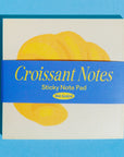 Sticky note pad with croissant design on a blue background
