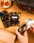 Leopard print phone case, sunglasses, and cleaning wipes on a beige surface