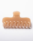 A single wide-tooth hair claw clip in a glossy, warm peach-beige translucent plastic, shown on a clean white background.