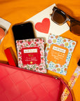 Phone, sunglasses, and 'well-kept' screen wipes on a bright orange surface with a red pouch.