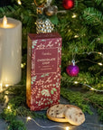 A box of Gifford's Chocolate Chip cookies stands on a dark surface in a festive holiday setting with lit candles, evergreen branches, string lights, ornaments, and two cookies in front.