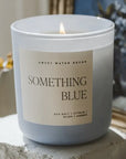 Candle labeled 'Something Blue' by Sweet Water Decor on a stone surface with a blurred background.