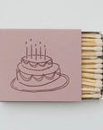 Matchbox with a pink cover featuring an illustration of a cake with candles on a white background