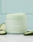 Jar of NCLA Beauty 'Hey Sugar' body scrub with cucumber slices on a light blue background