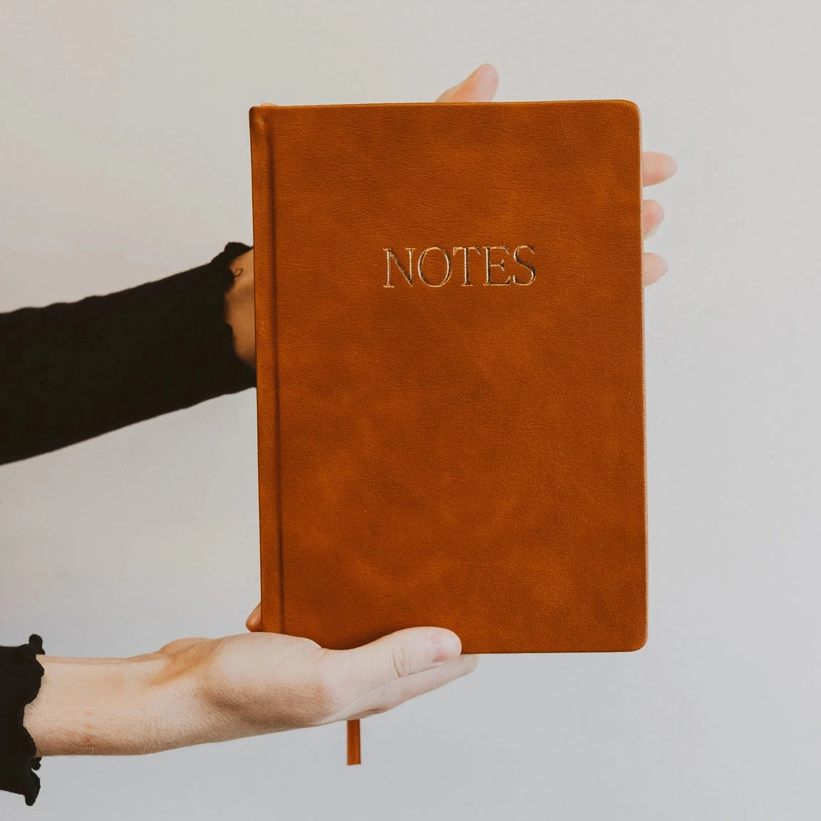 hands holding brown leather journal that says 'NOTES' on it in gold