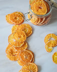 Dried orange slices on a marble surface with a jar of more dried oranges.