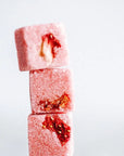 Three pink sugar cubes with red strawberry pieces on a white background