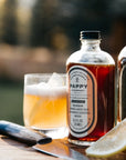 Pappy & Company cocktail mixer bottle with a glass of cocktail and lemon on a wooden surface.