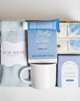 BOXFOX HEAL Gift Box with 2 magnesium packets, a travel hand cream, shower steamers, a minty tea sachet, a white ceramic mug, and light blue cozy socks