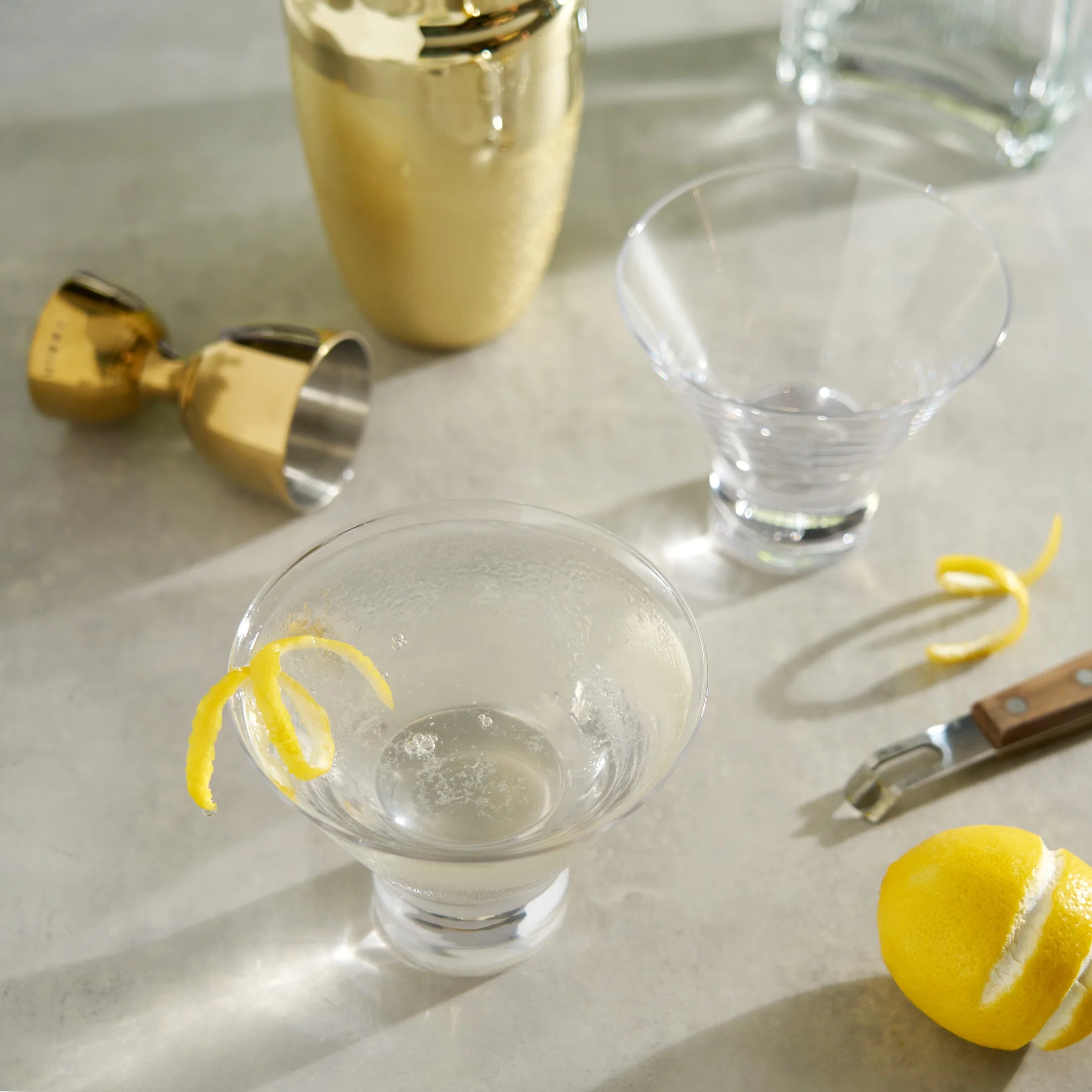Heavy Base Crystal Martini Glasses next to shaker, jigger, peeler and lemon twist