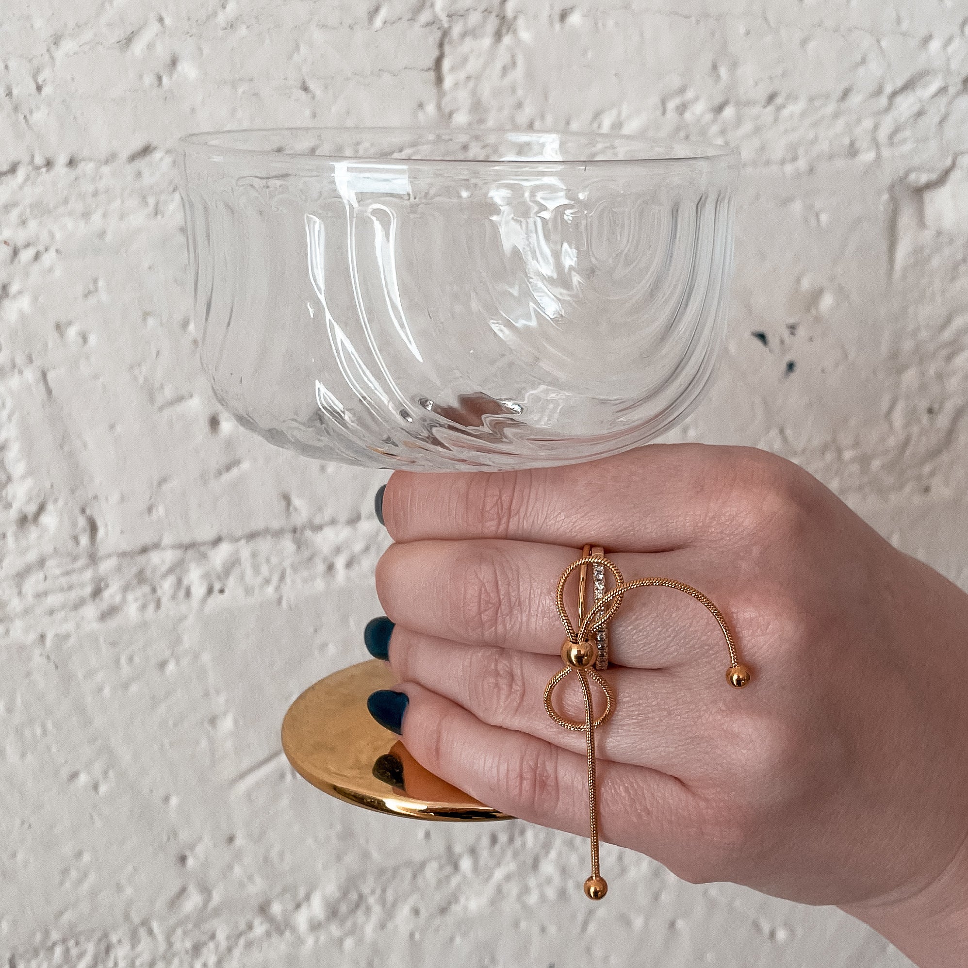 Gold bow ring on hand holding champagne coupe
