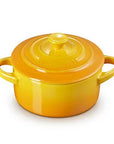 A small round enameled cast iron pot with lid, featuring a vibrant yellow-to-orange gradient glaze and double side handles, shown on a plain white background.