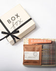 A curated gift box set from Box Fox, featuring a cream-colored gift box with a black ribbon and bow alongside tea and beauty items including a Tea With Tae packet and a pink New Beauty stick.