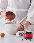 Person adding ingredients to a mixing bowl with a white background